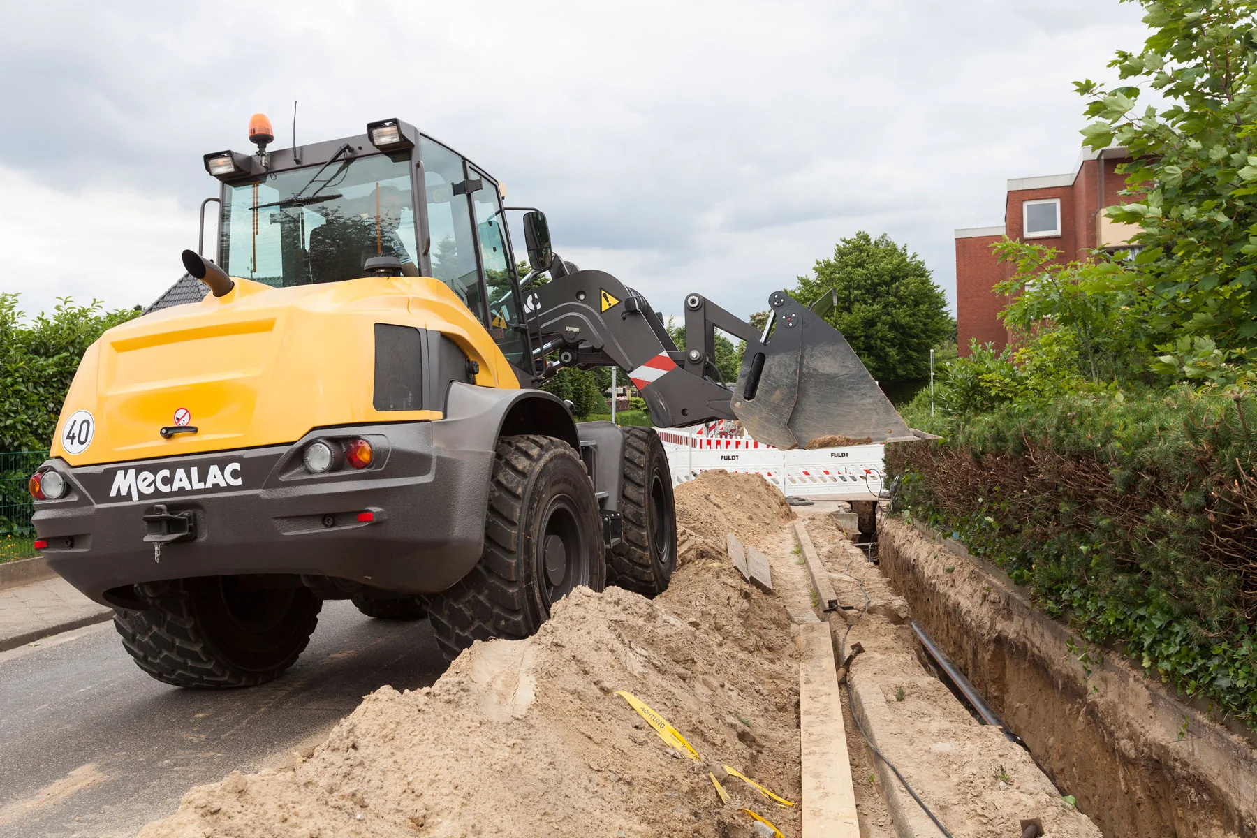 Mecalac AS1600 Schwenklader lädt Material neben einem Graben