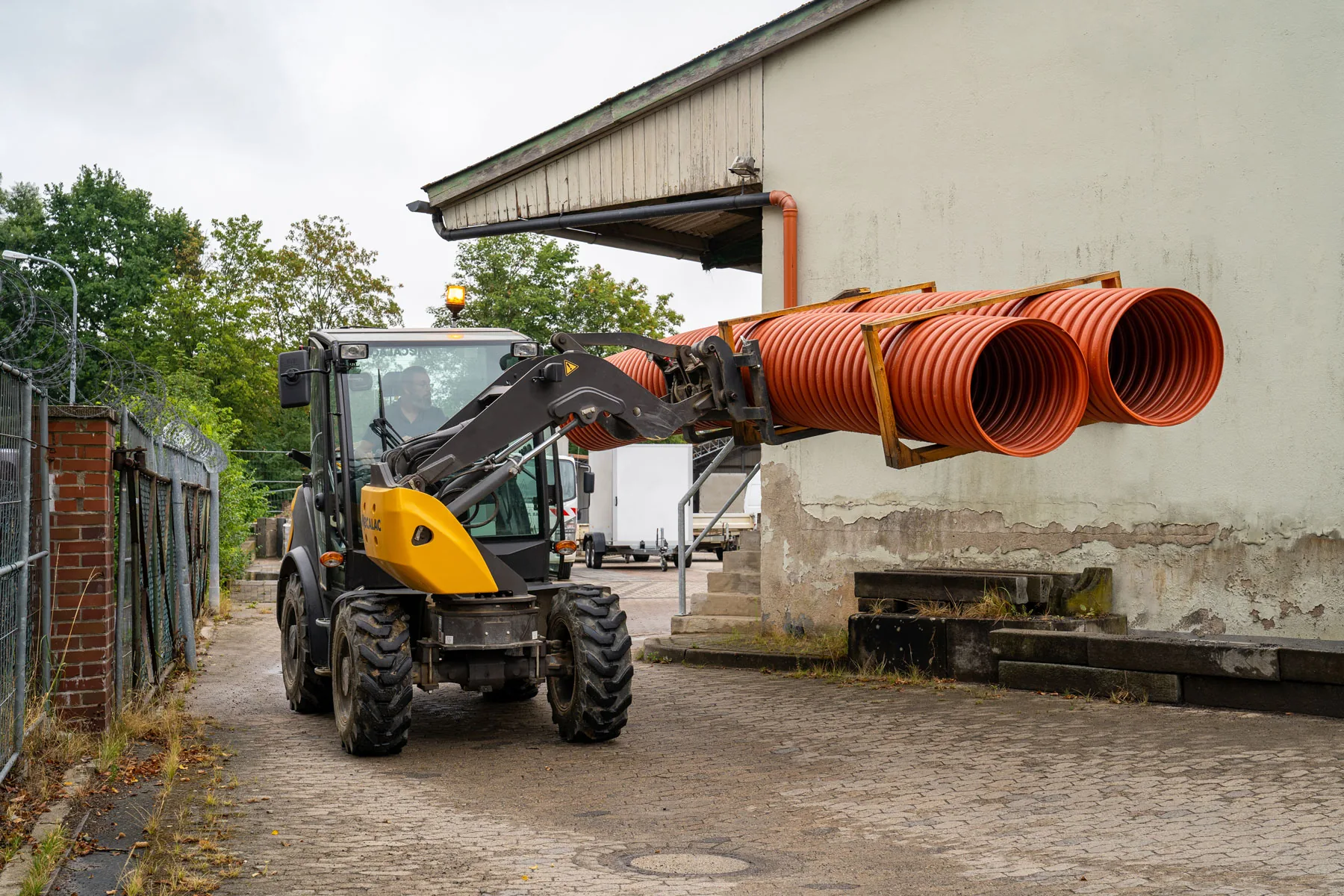 Mecalac AS600 Schwenklader transportiert große Rohrpakete auf einer Gabel